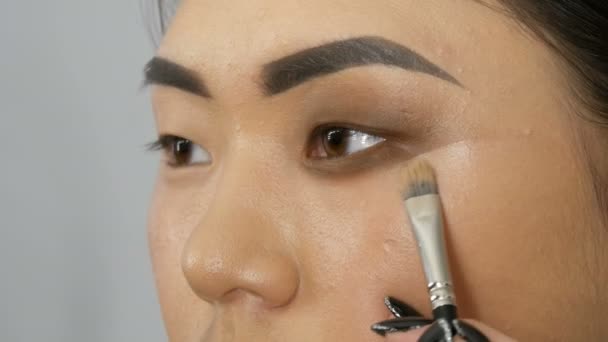 Artista de maquiagem estilista profissional compõe o olho fumegante de um rosto modelo de menina asiática no estúdio de visagem — Vídeo de Stock