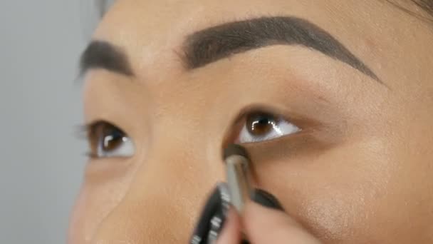 Επαγγελματίας στυλίστας make-up artist κάνει το smoky μακιγιάζ στα μάτια του ένα πρόσωπο μοντέλο ασιατικό κορίτσι στο visage studio — Αρχείο Βίντεο