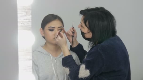 Professionele stylist Visagist maakt het rokerige oog van een Aziatische meisje in visage studio — Stockvideo