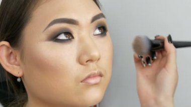 Profesyonel makyöz Asyalı kız modeli yüz görünümü kadar visage Studio yakın bir kapatıcı özel fırça ile uygulanır. Yüksek moda, studio video çekim