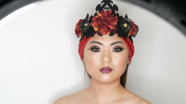 Alta moda, retrato de una hermosa modelo de chica asiática con maquillaje brillante en un turbante rojo y corona que está posando en un estudio de modelo profesional . — Vídeo de stock