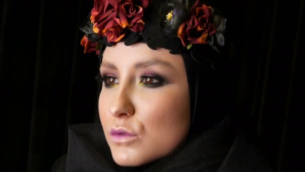 Professional girl model with beautiful makeup poses in a black cap and wreath on her head in front of the camera on black background in the image of a black widow. High-fashion — Stock Video