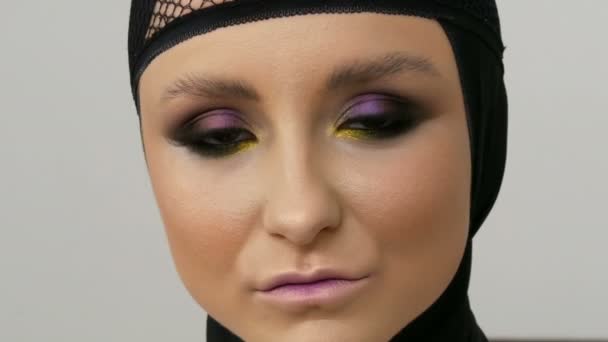 Νέος επαγγελματίας μοντέλο κορίτσι με όμορφο μακιγιάζ και καστανά μάτια που ποζάρει σε ένα μαύρο καπάκι στο κεφάλι της μπροστά από την κάμερα σε ένα λευκό φόντο στην εικόνα της μαύρης χήρας. Υψηλής μόδας. — Αρχείο Βίντεο