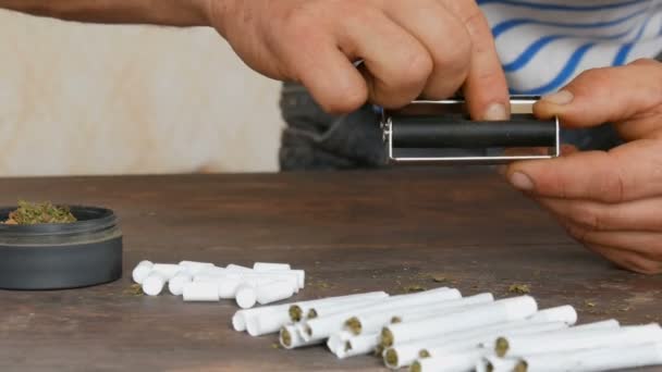 Mãos dos homens fazer cigarro artesanal ou roll-ups com máquina roll-up. Folhas esmagadas de tabaco e papel de cigarro de autoprodução de cigarros. Close up de mãos e charutos papel — Vídeo de Stock