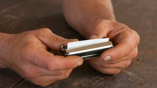 Mãos dos homens fazer cigarro artesanal ou roll-ups com máquina roll-up. Folhas esmagadas de tabaco e papel de cigarro de autoprodução de cigarros. Close up de mãos e charutos papel — Vídeo de Stock