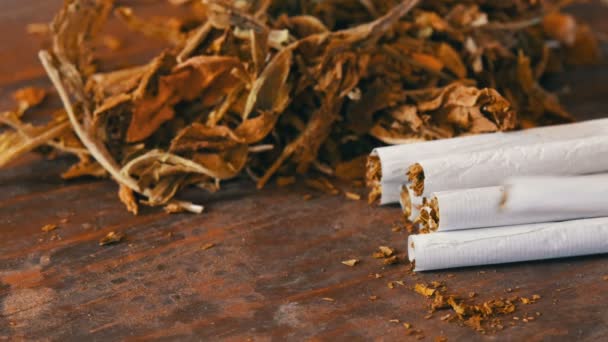 Domácí cigarety nebo roll-up s tabákem jsou na stole vedle suchých tabákových listů — Stock video