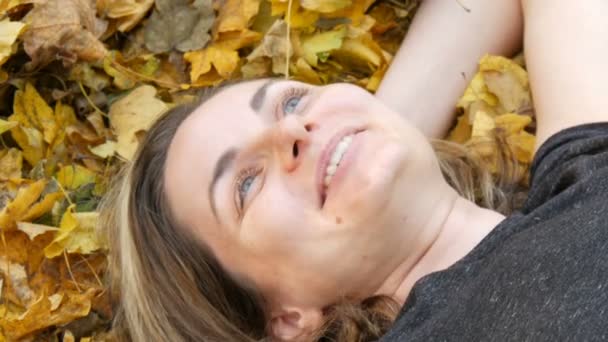 De cerca retrato de la cara de la hermosa joven sin maquillaje que se encuentra en el follaje amarillo de otoño y disfruta de la vida — Vídeos de Stock