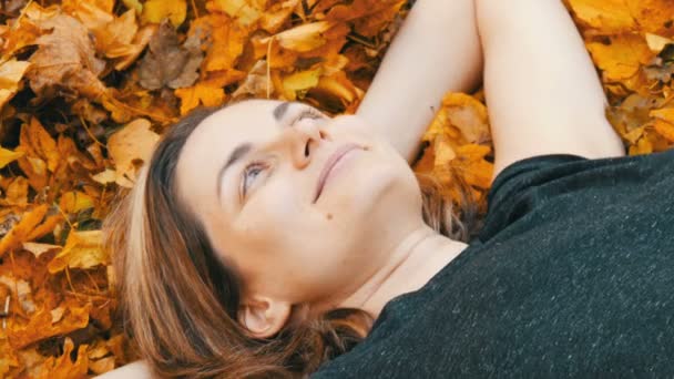 Portret van het gezicht van mooie jonge meisje zonder make-up die ligt in de herfst geel loof en geniet van het leven — Stockvideo