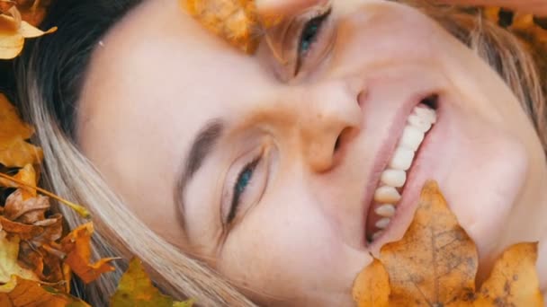 Close-up portret van het gezicht van mooie jonge meisje zonder make-up die ligt in de herfst geel gebladerte en geniet van het leven — Stockvideo