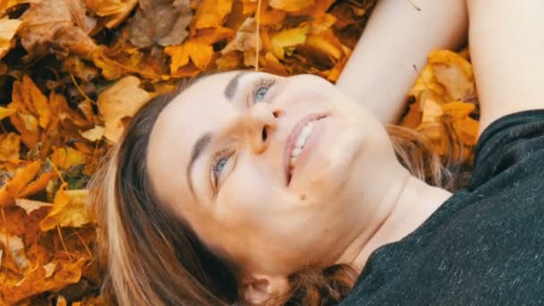 De cerca retrato de la cara de la hermosa joven sin maquillaje que se encuentra en el follaje amarillo de otoño y disfruta de la vida — Vídeos de Stock