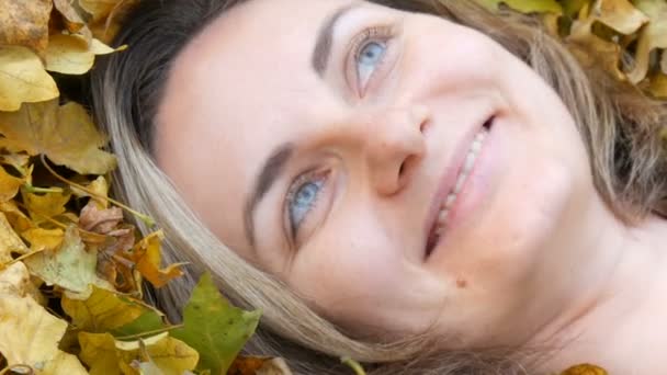 Закрыть портрет красивой молодой девушки без макияжа, которая лежит в осенней желтой листве и наслаждается жизнью — стоковое видео