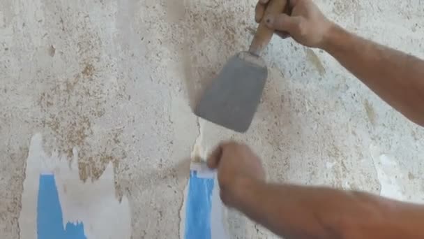 Человек очищает глиняные стены от старых обоев с помощью лопатки крупным планом — стоковое видео