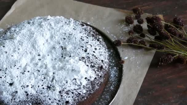 W domu świeżo pieczone Piernik czekoladowy placek upudrował pudrem cukrem leży obok stylowe łąka suszonych kwiatów — Wideo stockowe
