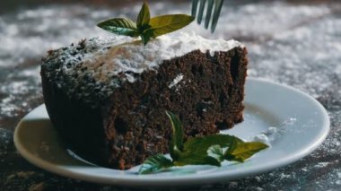 Ev yapımı fırında çikolatalı browni kek beyaz bir tepside pudra şekeri ile boğuk nane yaprakları ile süslenmiş. Dilim kek pasta plaka kapalı çatal tatili