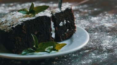 Ev yapımı fırında çikolatalı browni kek beyaz bir tepside pudra şekeri ile boğuk nane yaprakları ile süslenmiş. Dilim kek pasta plaka kapalı çatal tatili