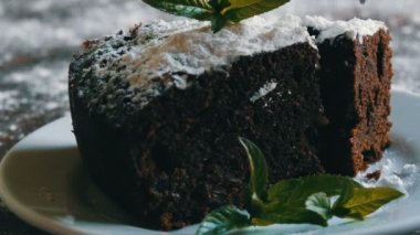 Ev yapımı fırında çikolatalı browni kek beyaz bir tepside pudra şekeri ile boğuk nane yaprakları ile süslenmiş. Dilim kek pasta plaka kapalı çatal tatili