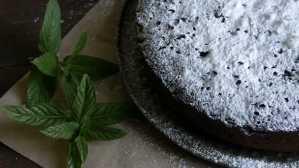 Elegante pastel de chocolate horneado casero generosamente en polvo con un azúcar glaseado junto a hojas de menta fresca — Vídeo de stock