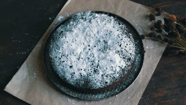 Домашній свіжоспечений шоколадний пиріг з борделі, покритий глазурованим цукром, лежить поруч зі стильними сушеними луговими квітами — стокове відео