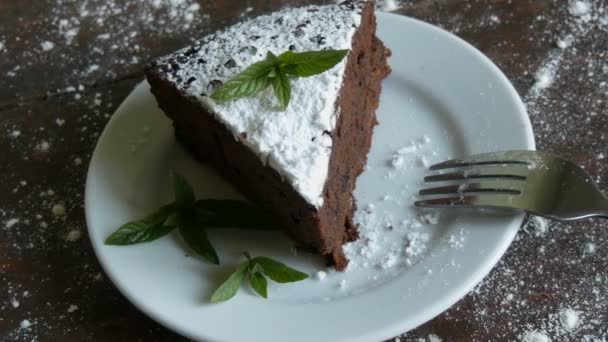 Een stukje chocolade brownie cake op een witte plaat versierd met verse muntblaadjes naast de vork — Stockvideo