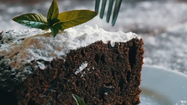 Ciasto domowe pieczone Piernik czekoladowy stłumiony z cukrem pudrem na białym talerzu urządzone z liści mięty. Widelec zrywa kawałek tortu brownie z płytki — Wideo stockowe