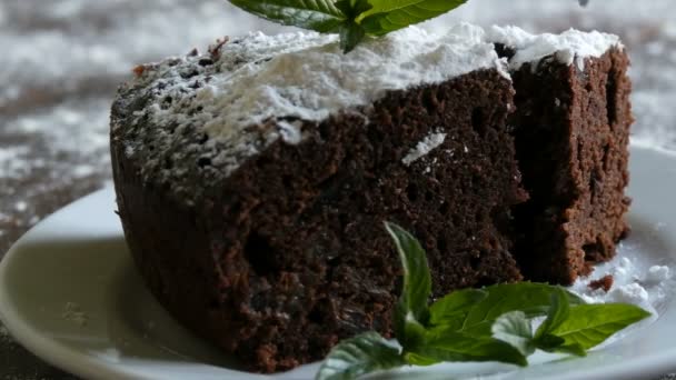 Pastel de chocolate horneado casero de brownie amortiguado con azúcar en polvo en un plato blanco decorado con hojas de menta. Tenedor rompe pedazo de pastel de brownie de la placa — Vídeo de stock