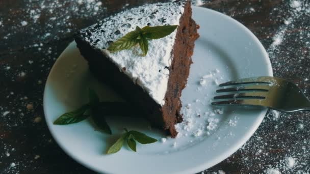 Een stukje chocolade brownie cake op een witte plaat versierd met verse muntblaadjes naast de vork — Stockvideo