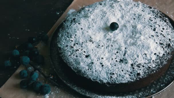 Pastel de chocolate brownie generosamente cubierto con azúcar glaseado con estilo acostado junto a las bayas azules. La mano femenina decora las bayas pastel casero — Vídeo de stock