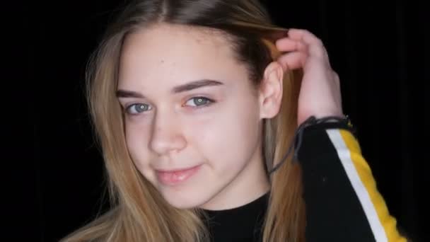 Portret van een mooie jonge tiener meisje met lange witte haren en groene ogen poseren gek rond glimlachen en het aanraken van haar haar in de voorkant van de camera in de studio op een zwarte achtergrond — Stockvideo