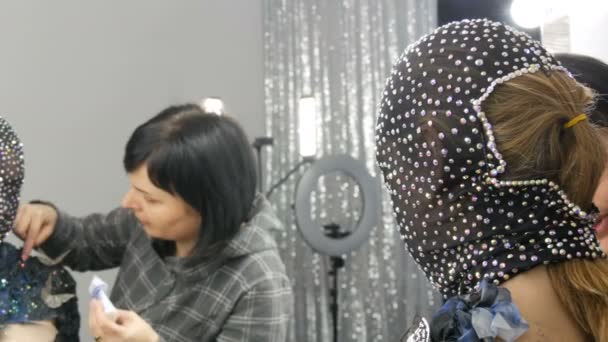 Висока мода. Дизайнер готує зображення дівчини-інопланетянки в чорній масці в блискучих стразах, блискітках, металевих метеликах в студії перед дзеркалом — стокове відео