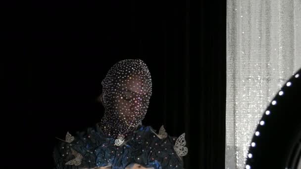 High-fashion. Model in the image of an alien girl in a black mask in sparkling rhinestones, sparkles, metal butterflies on a black and silver background posing in a model studio. — Stock Video