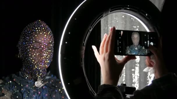 Hochmodisch. Modell im Bild eines fremden Mädchens mit schwarzer Maske in glitzernden Strasssteinen, Funkeln, Metallschmetterlingen auf schwarz-silbernem Hintergrund, die in einem Modelstudio posieren. — Stockvideo