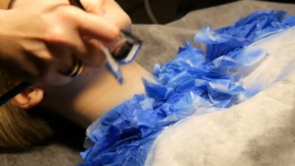 Estúdio de moda, o modelo está se preparando para o show. Adolescente jaz em um sofá especial, designer prepara sua imagem usando um spray de aerógrafo especial com tinta azul — Vídeo de Stock