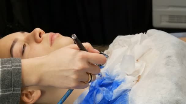 Στούντιο μόδας, το μοντέλο ετοιμάζεται για την παράσταση. Teen κορίτσι βρίσκεται σε ένα ειδικό καναπέ, σχεδιαστής προετοιμάζει την εικόνα της χρησιμοποιώντας ένα ειδικό σπρέι αερογράφου με μπλε χρώμα — Αρχείο Βίντεο