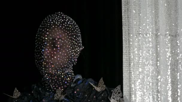 Yüksek moda. Bir model stüdyosunda poz siyah ve gümüş arka planda parlayan Rhinestones, parıltılı, metal kelebekler siyah bir maske bir uzaylı kız görüntü modeli. — Stok video