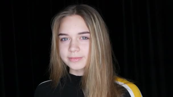 Πορτραίτο ενός όμορφου νεαρού κοριτσιού με μακριά λευκά μαλλιά και πράσινα μάτια που ποζάρουν χαμογελώντας και αγγίζοντας τα μαλλιά της μπροστά από την κάμερα στο στούντιο σε μαύρο φόντο — Αρχείο Βίντεο
