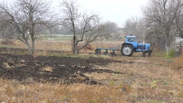 Голубой трактор вспахивает стальные борозды в конце осени в поле — стоковое видео