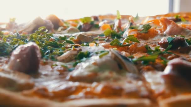 Een grote vers gebakken pizza waarmee er stoom is, een dicht uitzicht. Heerlijke pizza met tomaat, greens, Beierse worstjes, champignons, spek. — Stockvideo