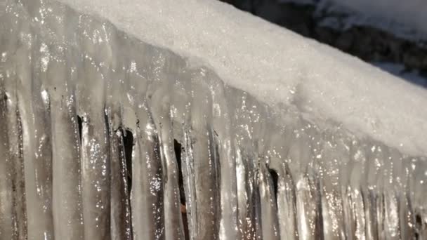 Huge thick icicles hanging from the roofs are melting under spring sun — Stock Video