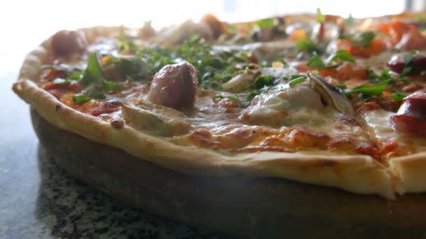 A nagy, frissen sült pizzát, amely a gőz, a közeli kilátás. Ízletes pizza paradicsom, zöldek, bajor kolbász, gomba, bacon. — Stock videók