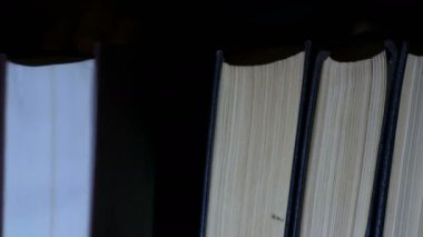 Bir kitap sıraya alınır. Kütüphanede bir kitaplıkta büyük eski kitapların satırı.