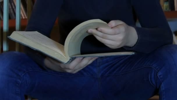 Adolescent garçon lit un livre dans l 'bibliothèque sur un fond de bibliothèques avec beaucoup de livres fermer — Video