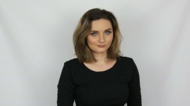 Güzel genç seksi kadın siyah elbise onaylayarak sevgi ile nazikçe ve gülümseyerek kamera içine beyaz bir arka planda stüdyo bakıyor.