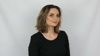 Güzel genç seksi kadın siyah elbise onaylayarak sevgi ile nazikçe ve gülümseyerek stüdyo beyaz bir arka planda bakıyor.