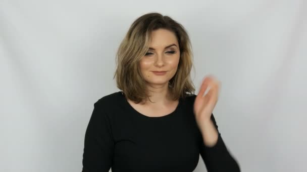 Retrato de una hermosa joven sexy mujer elegante en un vestido negro que toca su cabello, endereza su cabello y mira a la cámara mientras sonríe sobre un fondo blanco . — Vídeos de Stock