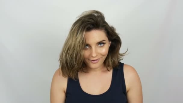 Portrét krásné mladé sexy elegantní ženy v černých šatech, které se jí dotýkala vlasů, se usilovně dotkne vlasů a dívá se do kamery při úsměvu na bílém pozadí. — Stock video