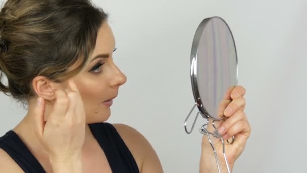 Portrait d'une belle jeune femme qui regarde dans un grand miroir rond sur fond blanc dans le studio — Video
