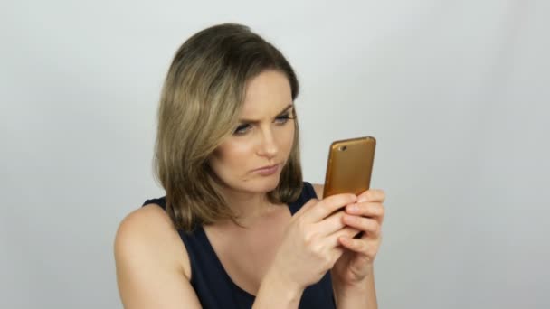 Portrait d'une belle jeune femme qui pose faisant un selfie et communiquant et regardant dans un smartphone qui tient dans ses mains sur fond blanc en studio — Video