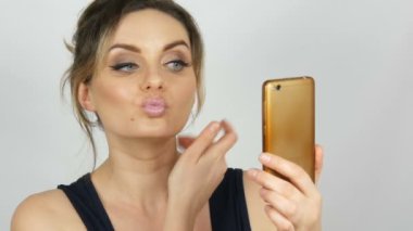 Bir selfie yapma ve iletişim ve stüdyoda beyaz arka planda elinde tutan bir akıllı telefona bakarak poz veren güzel bir genç kadının portresi