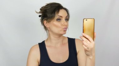 Bir selfie yapma ve iletişim ve stüdyoda beyaz arka planda elinde tutan bir akıllı telefona bakarak poz veren güzel bir genç kadının portresi