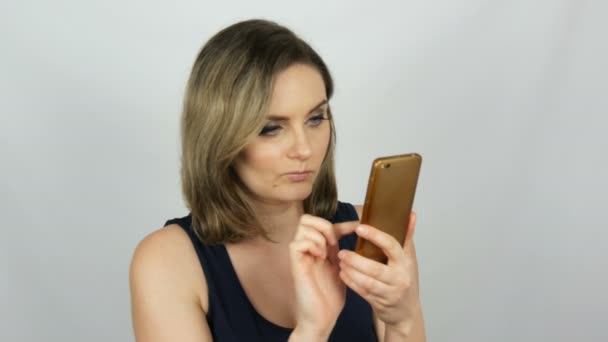 Retrato de una hermosa joven que está posando haciendo una selfie y comunicándose y mirando en un teléfono inteligente que sostiene en sus manos sobre fondo blanco en el estudio — Vídeos de Stock